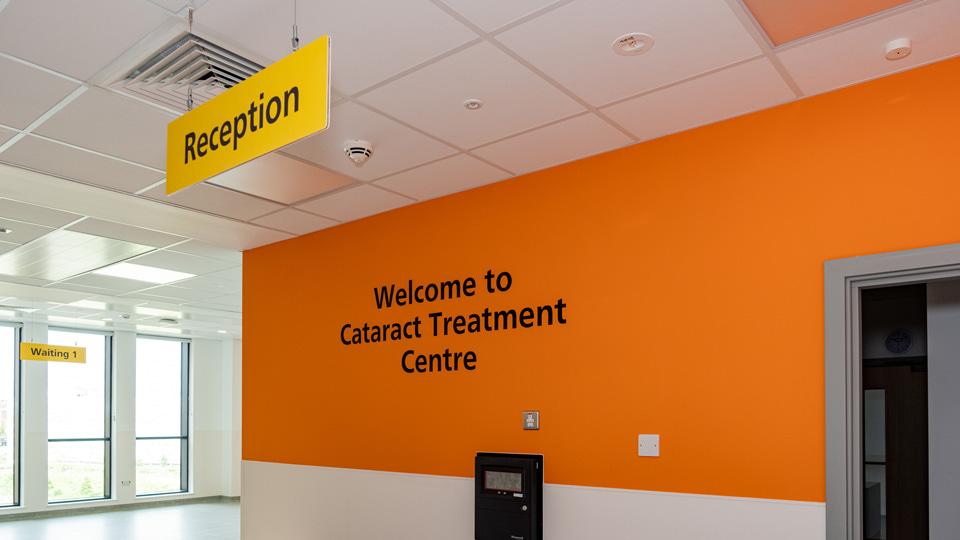 The reception to the Cataract Treatment centre has a white and orange wall and bold welcoming signs