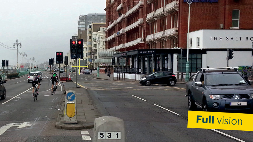 A busy road in a coastal town, with two lines of traffic moving both towards and away from the camera