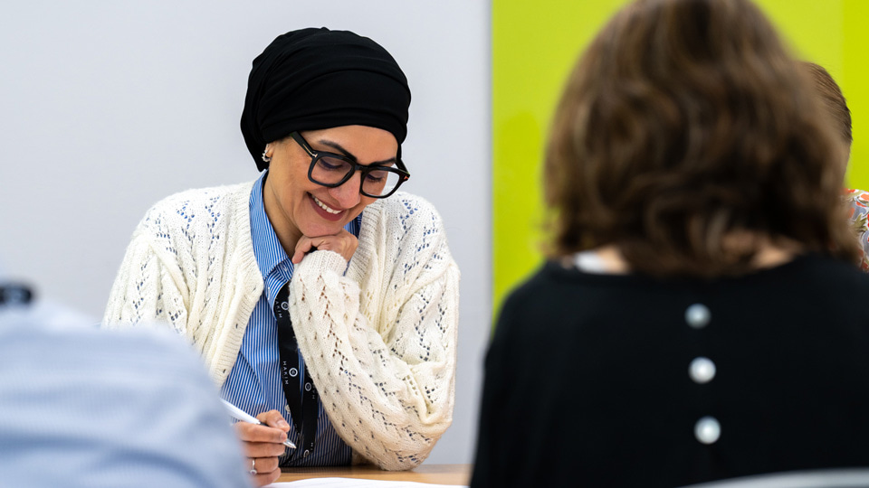 A woman smiles down at her notes, she is seated around a table with others