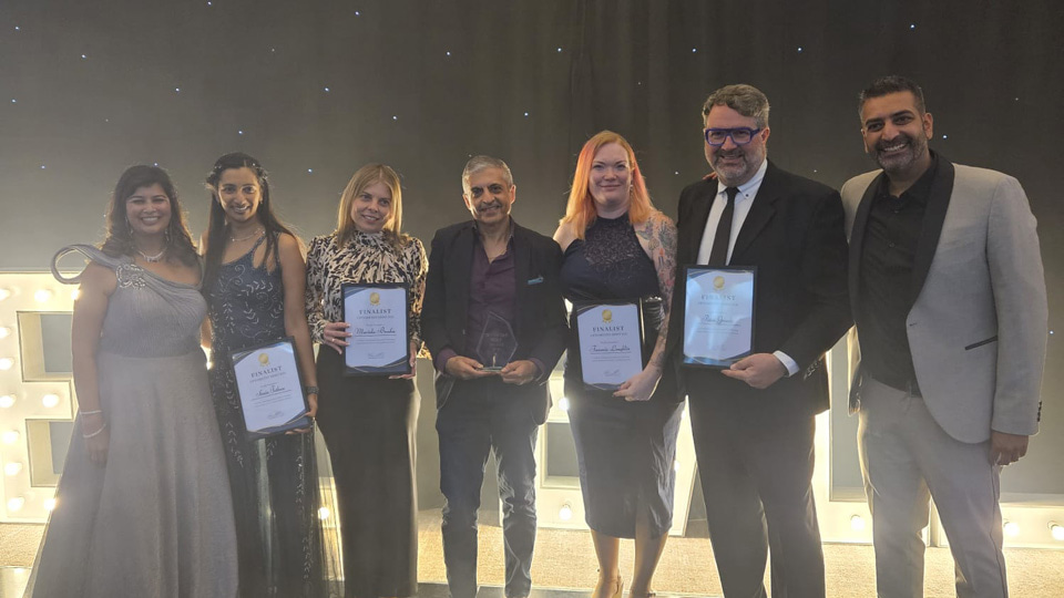 Four runners up and the winner of the Optometry Hero Award 2026 stand together holding certificates and trophies. They are all dressed formally. At each end stand Sheena and Piyus