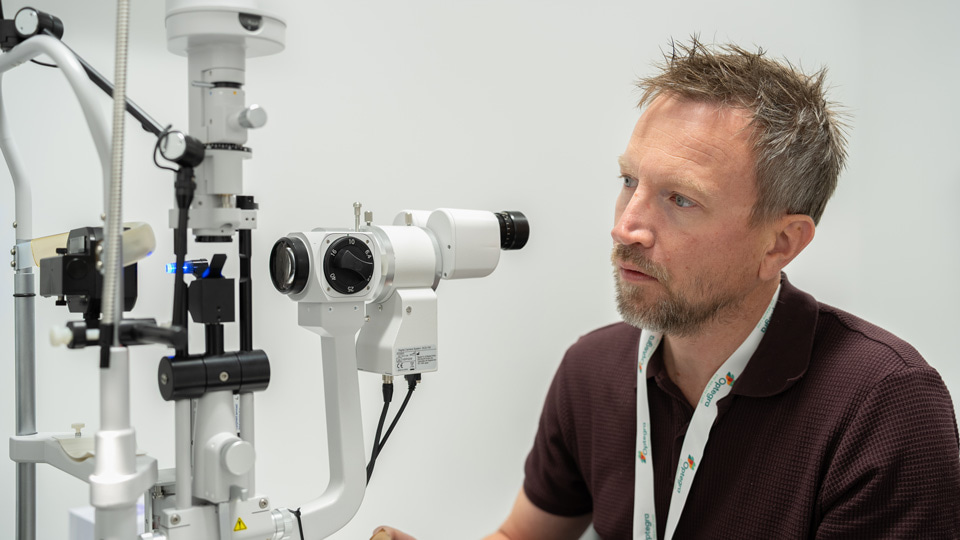 A man is seated at a slit lamp