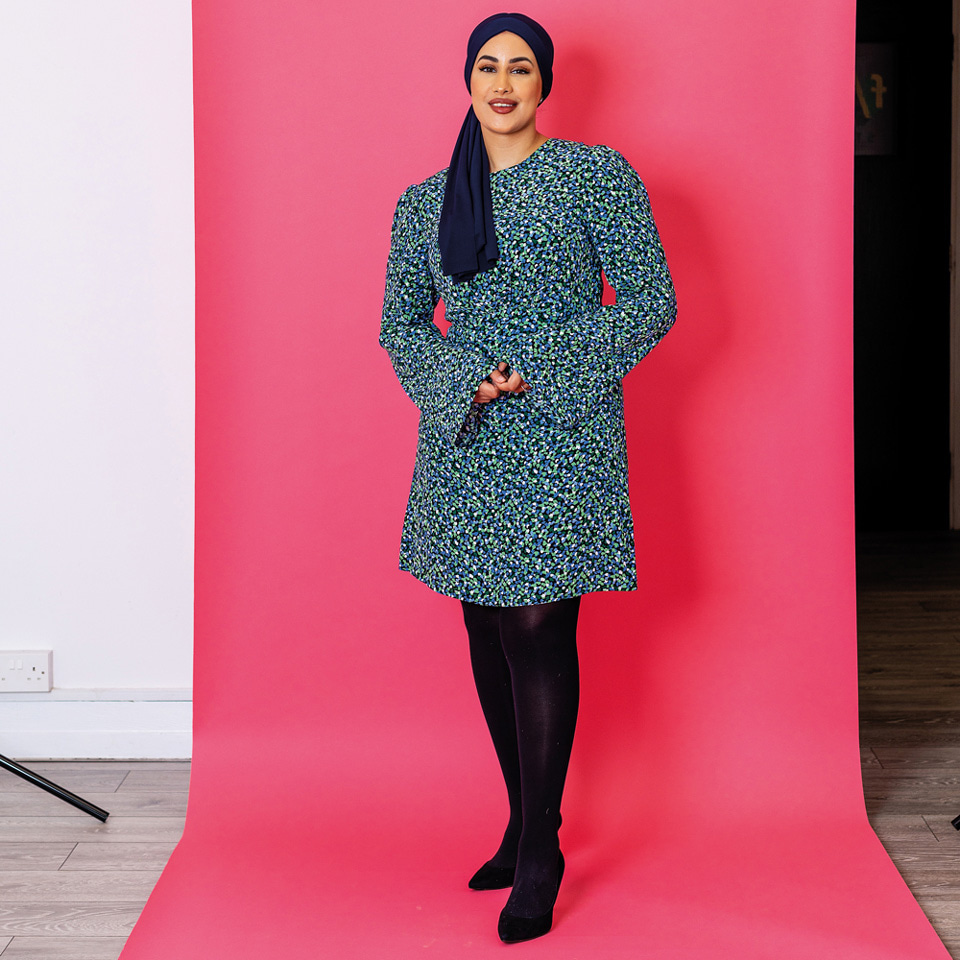 Full body shot of a woman wearing a blue dress standing in front of bright pink screen