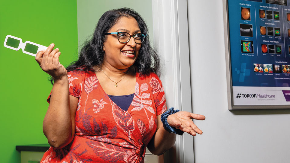 Bhavina Patel smiles while gesturing with a trial frame with coloured lenses
