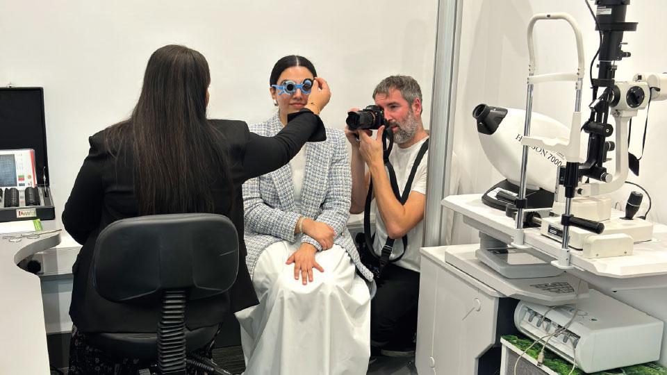 Optometrist Rashida Shaikh puts a trial frame in front of a patient while photographer Mark Newton photographs her