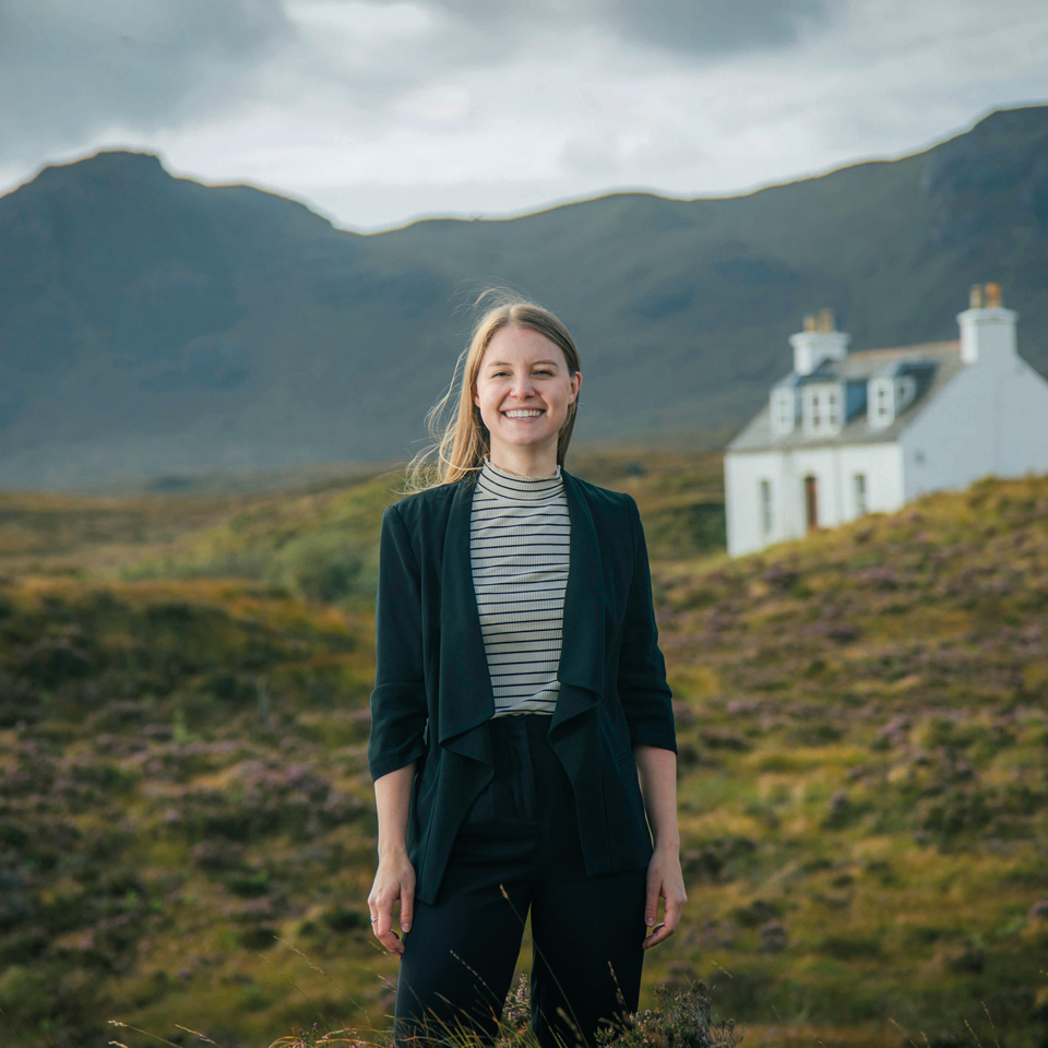 Optometrist Hannah Einarson is photographed with hills and a white house in the background on the Isle of Skye
