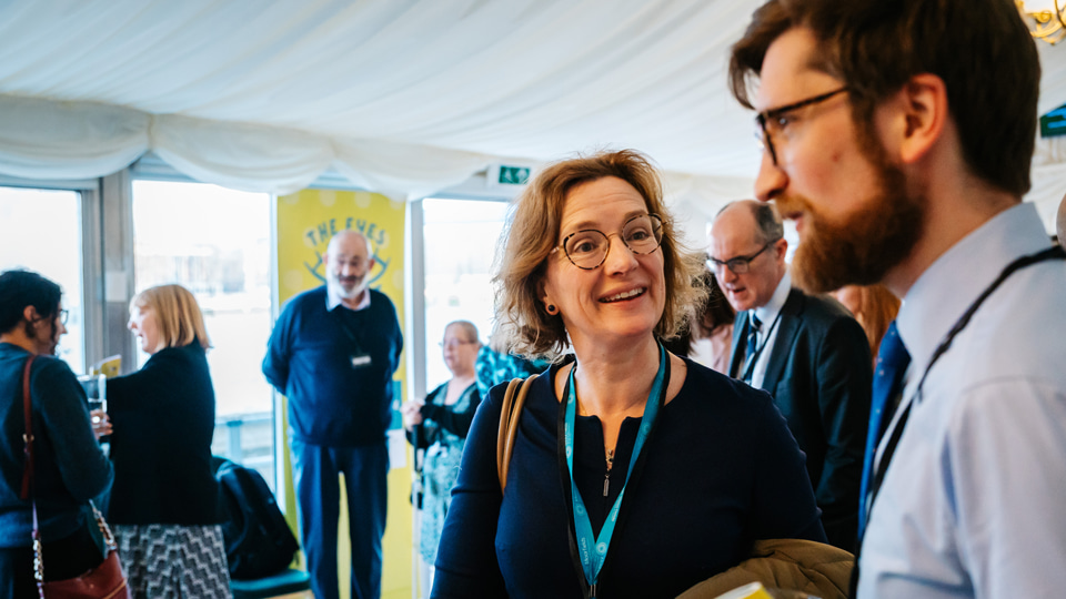 A woman with blonde hair talking to a man with brown hair and glasses at the event 