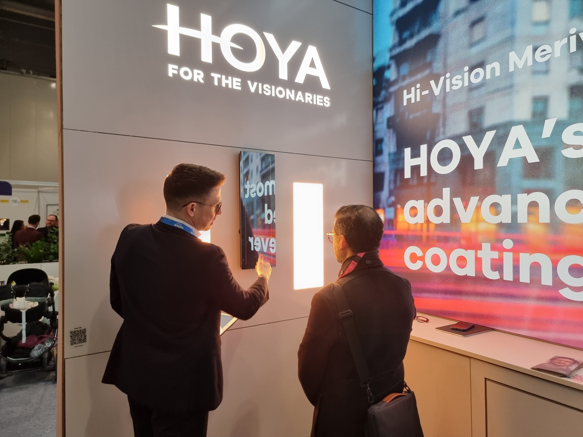 A photograph taken of the Hoya stand at a previous 100% Optical event, with a Hoya team member presenting to a delegate