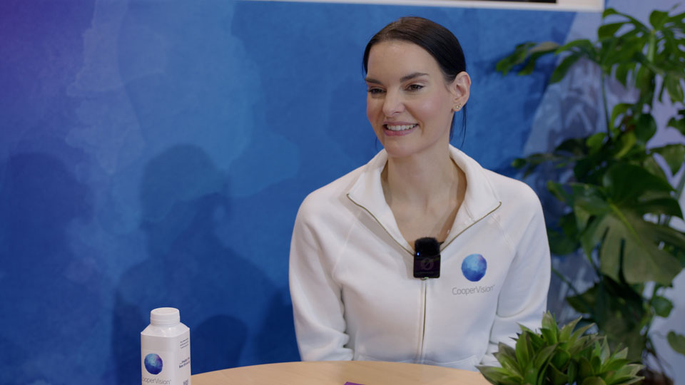 Christina Olner wears a branded CooperVision shirt and is seated on the manufacturer’s stand at 100% Optical