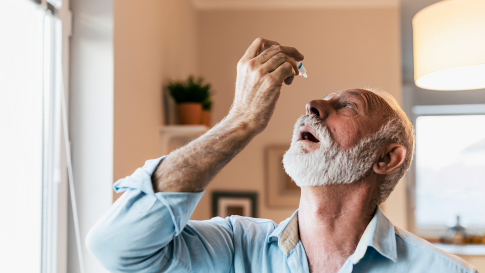 Senior man with a white beard using eye drops