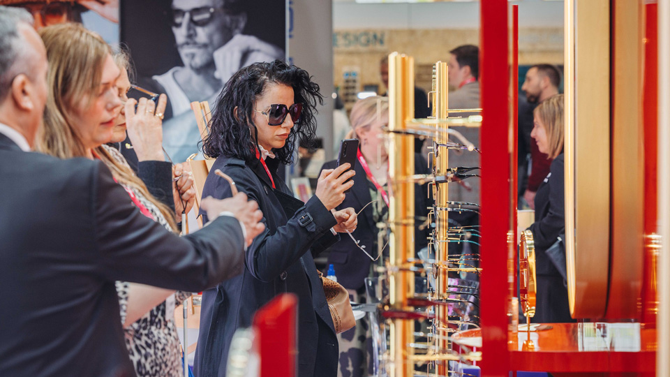 In a busy exhibition stand, a woman looks at an eyewear display