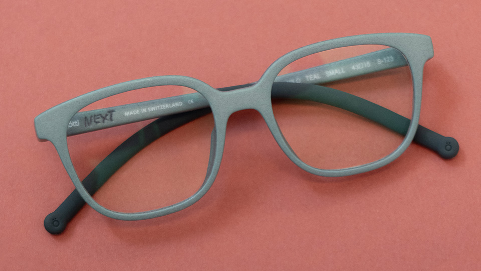 Three glasses in a matte teal, navy, and blush red are laid out on a red background