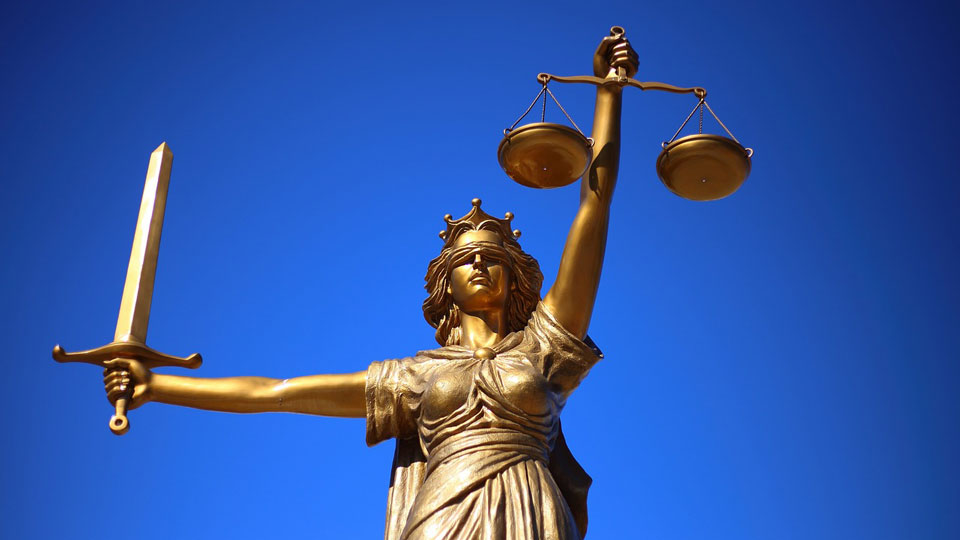 A gold lady of justice statue carries a set of scales and a sword 