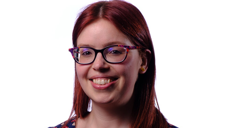 Dr Lindsay Rountree wears a smart patterned dress in red and blue and colourful spectacles