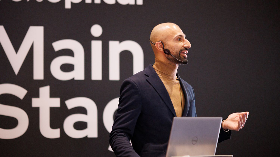 A speaker on the Main Stage at 100% Optical mid-presentation
