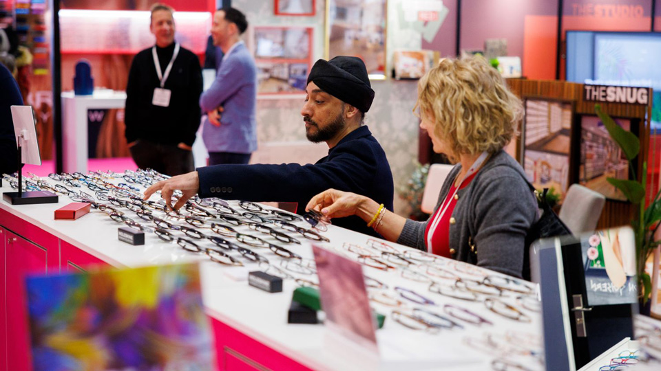 Two people look through a table of frames at an exhibition stand