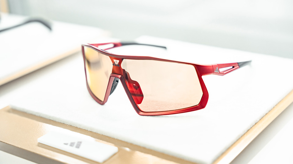A sporty slimline wrap frame in a red metal with orange tinted lenses is posed on a display board