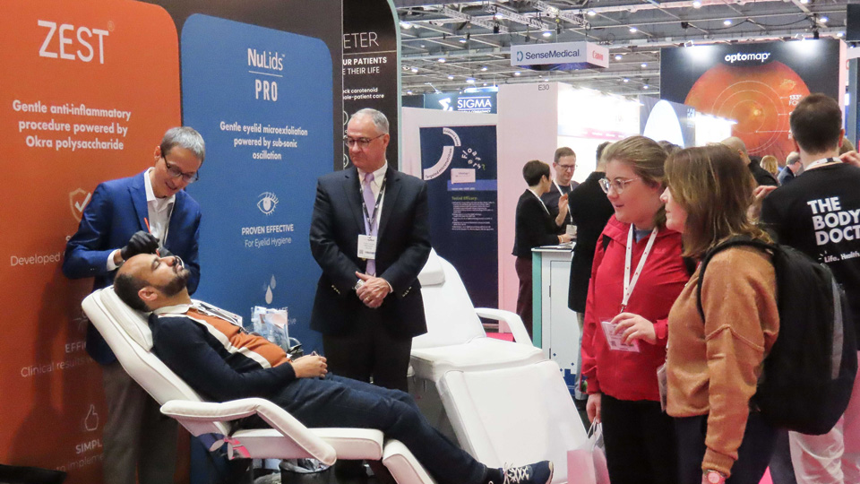 At a previous 100% Optical show, the founder of ZEST performs a demonstration of an eyelid cleaning tool while other delegates look on in interest