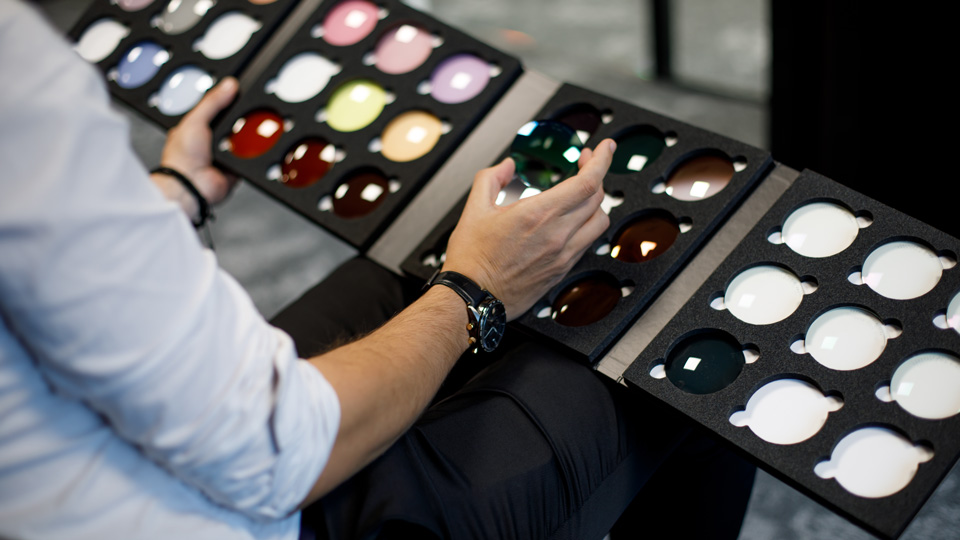 A man holds open a folding case of lenses of varying colours and tints open on his lap