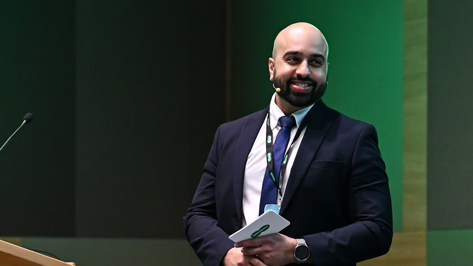 Bhavik Parmar stands on stage giving a presentation. He is smiling widely and wears a smart navy suit