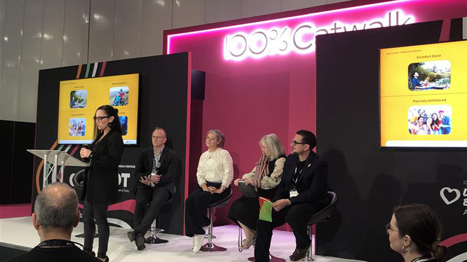 Natasha presents from a podium on the 100% Optical Catwalk, behind her are a panel of four people