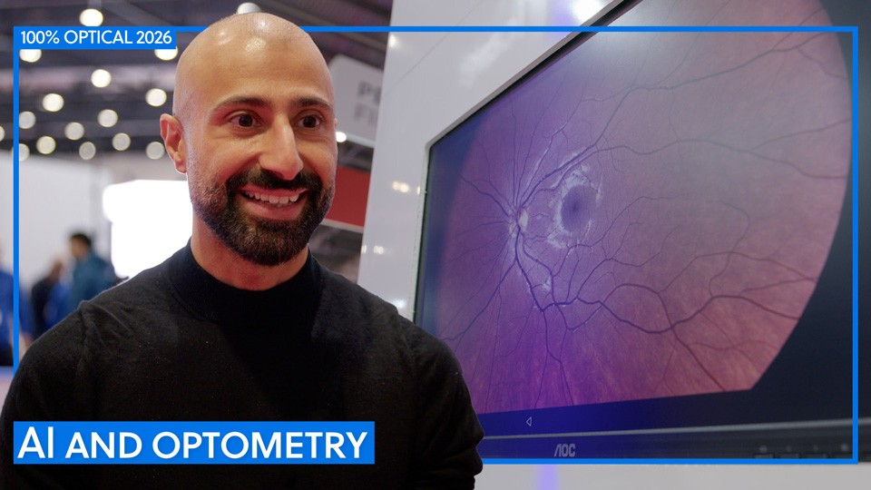 Kishan Devraj, in a black turtleneck, is photographed by a screen with a large image of the inside of an eye