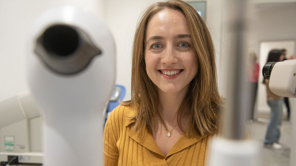 Josie poses behind optical equipment in a practice room