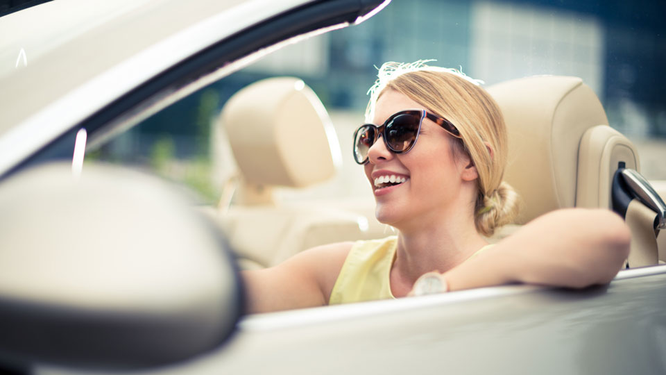 A female driver smiles wearing sunglasses in a convertible