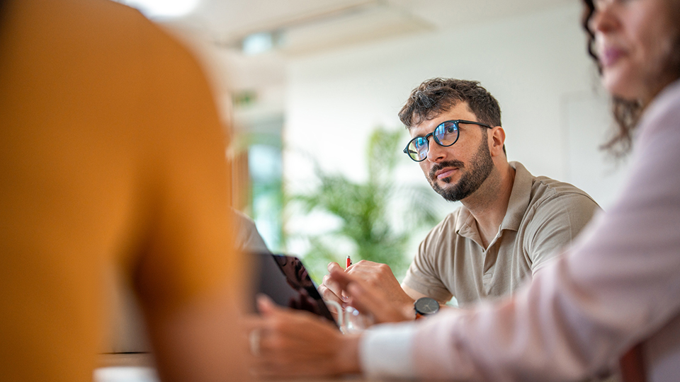 A man wearing glasses speaks with colleagues at a table