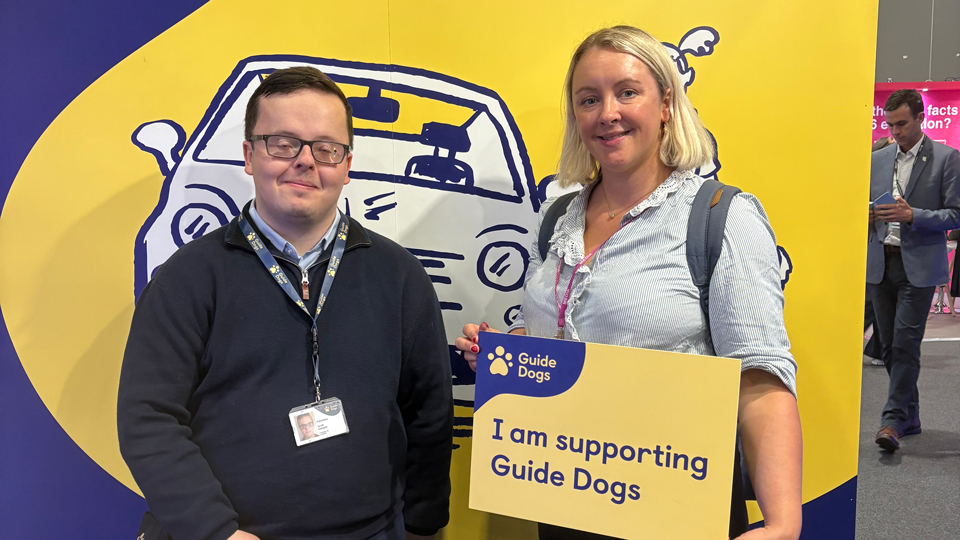 Lucy Miller holding a pledge placard alongside Scott Keegan, Guide Dogs volunteer, and his guide dog