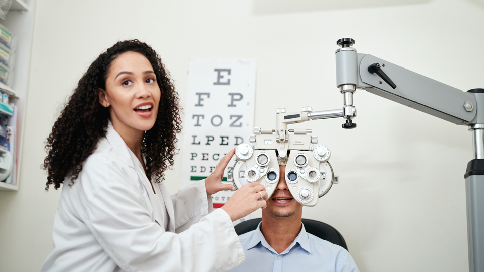 Young female optometrist facing the camera in front of an Amsler chart whilst giving a male patient an eye test 