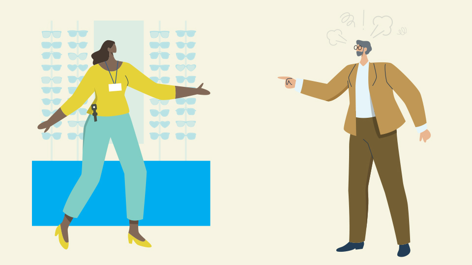 An angry customer points their finger at an eye care profesional standing in front of a spectacle display