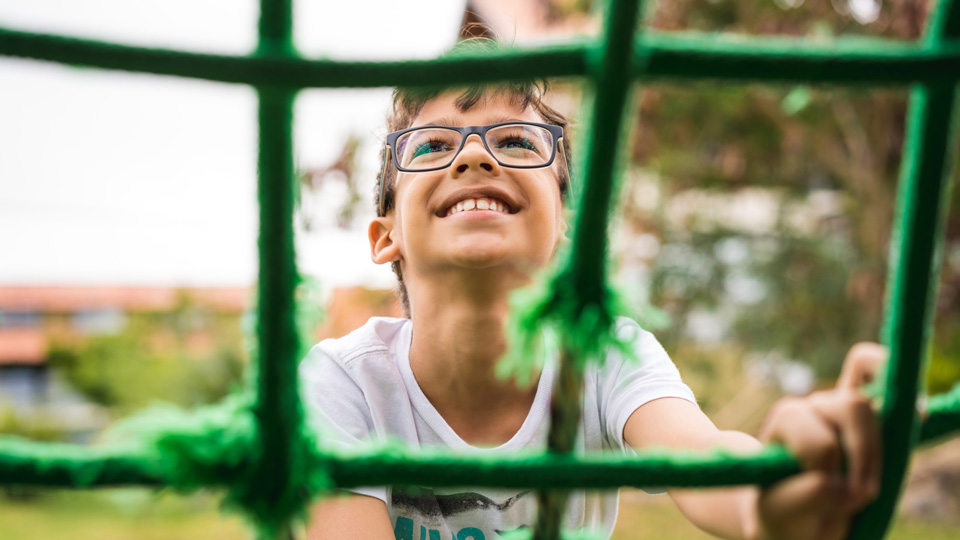 A boy wearing spectacles and smiling climbs a rope course 