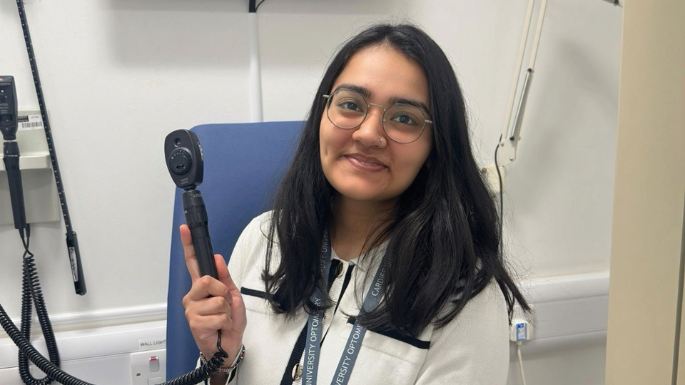 Heer is photographed in a clinical setting holding up a tool and smiling