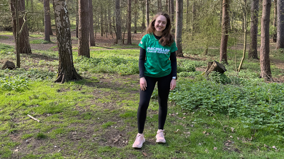 Josie wears athletic attire including a Macmillan branded running vest. She is photographed in a forest