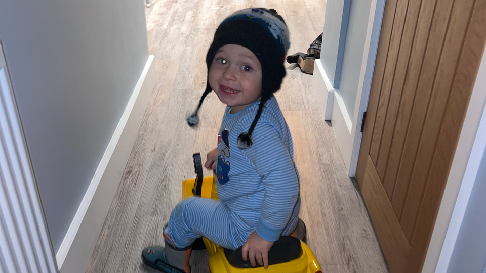 A toddler rides on a toy truck and looks back to the camera. One of his eyes glows white