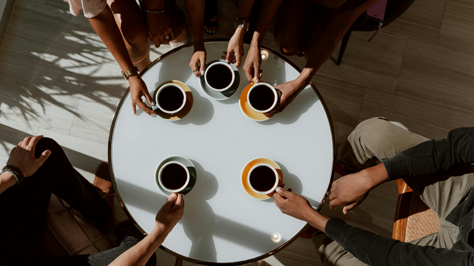 A top-down view of five people seated around a circular table, each holding coffee cups