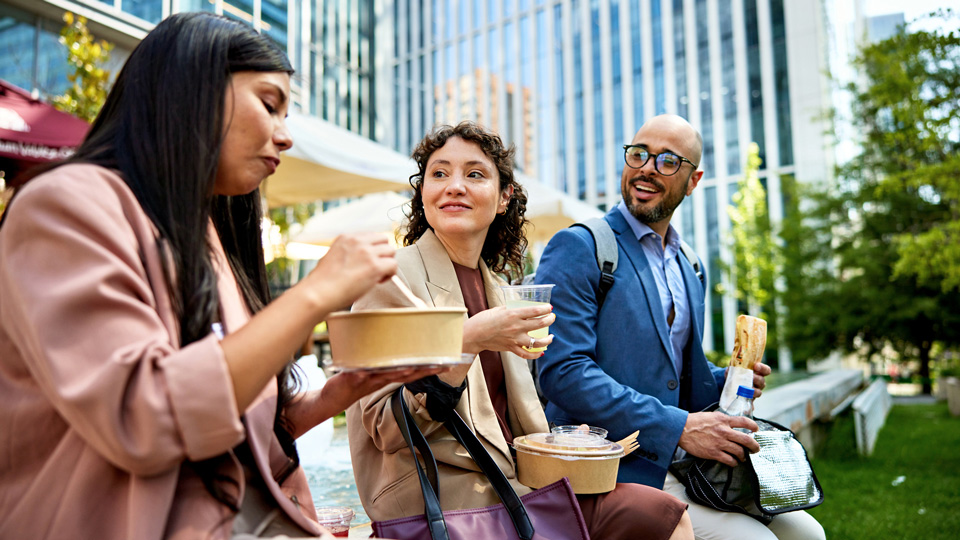 A group of professional colleagues chat outside over lunch