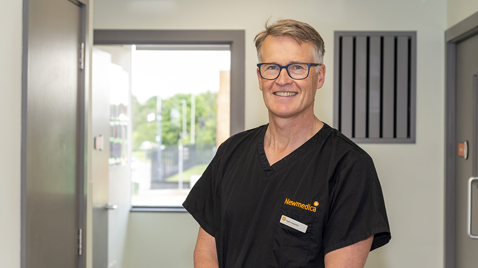 Nigel Kirkpatrick in blue scrubs smiling at the camera