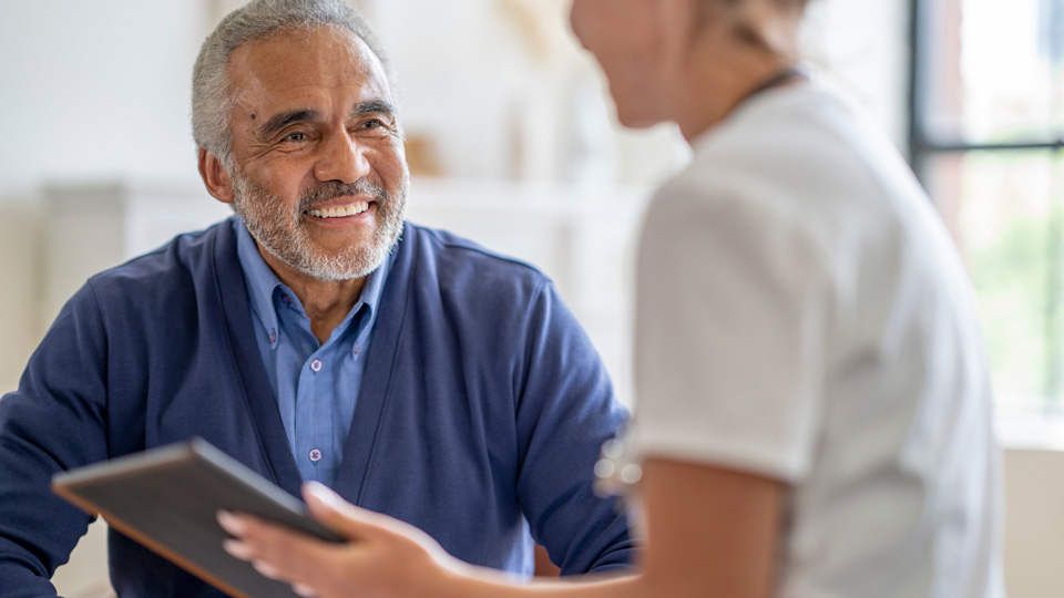 An older man smiles while speaking with a younger clinician