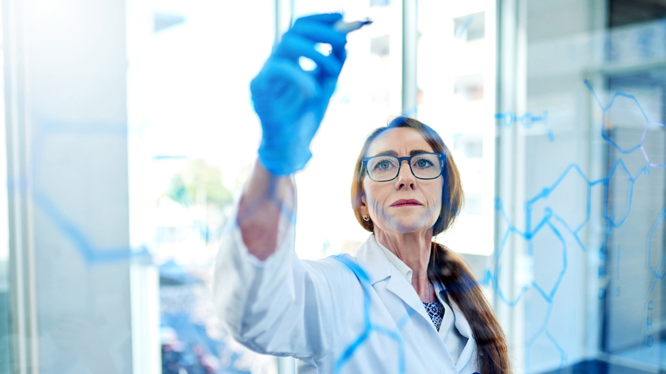 A female scientist draws on a transparent white board facing the camera