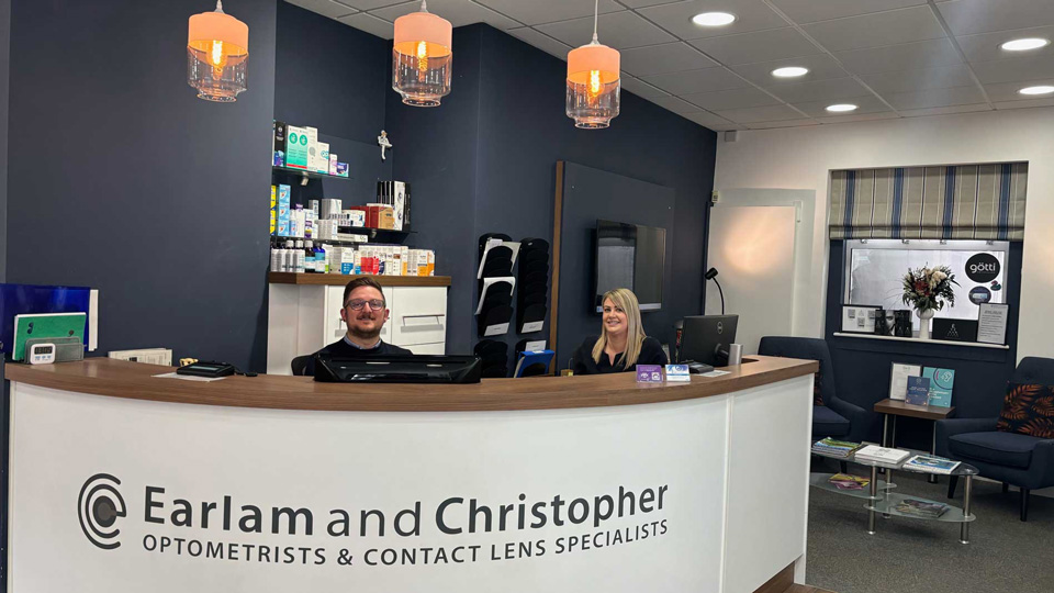 Two front of house staff sit behind a large curved reception desk for Earlam and Christopher