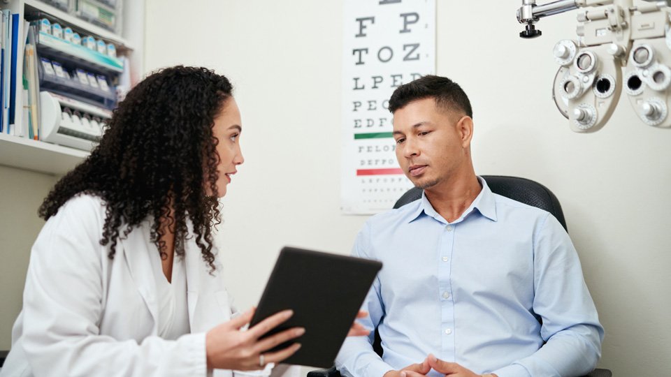 Optician with man sitting in testing room consulting about vision