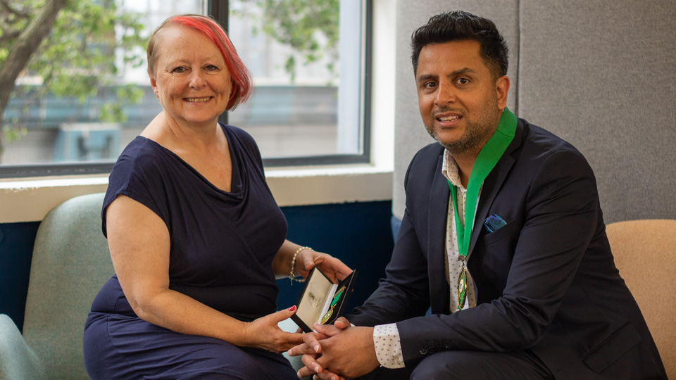 Emma Spofforth and Nizz Sabir sitting on an sofa holding the AOP chairman medal