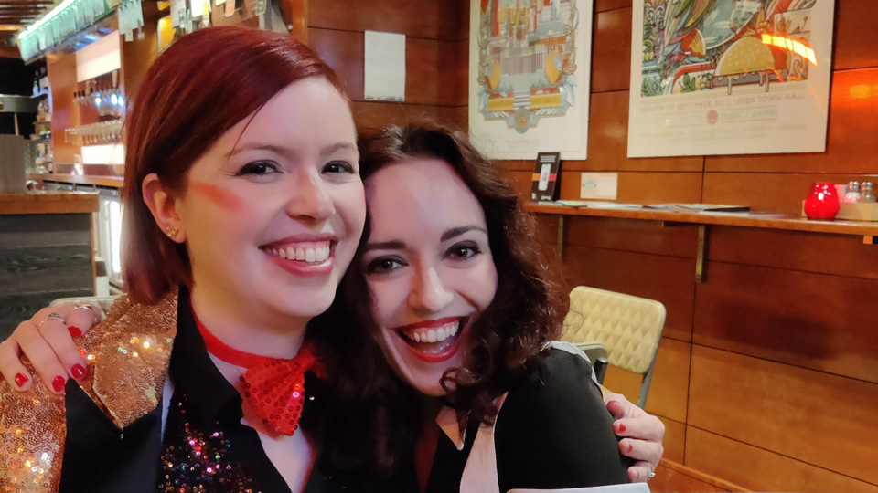Two women, Dr Lindsay Rountree, and Dr Sam Strong, in costume. Lindsay wears a sparkly top and jacket , while Sam has dark make up and a black and white dress