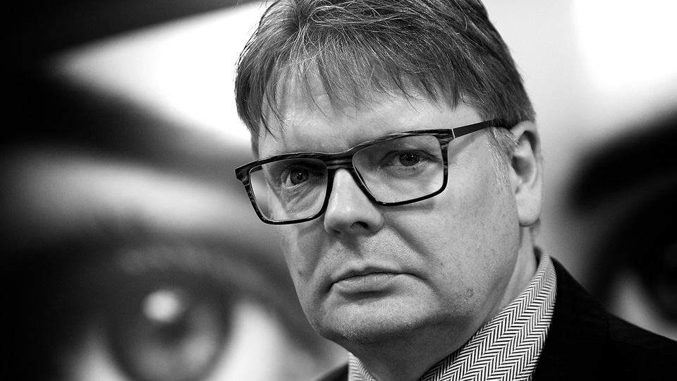 Black and white image of Nick Rumney looking at the camera whilst wearing a suit