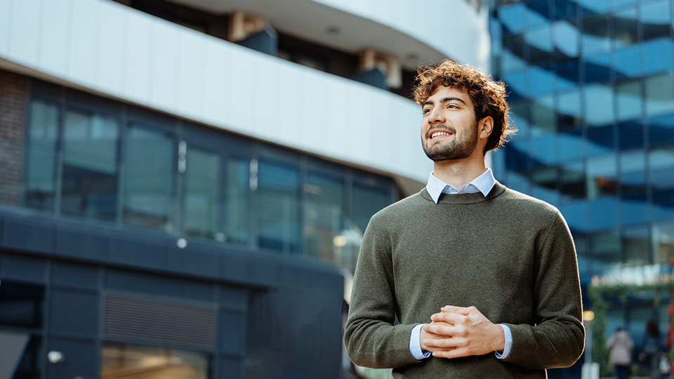 A young professional stands outside in an urban landscape