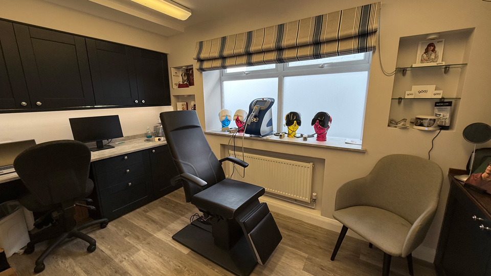 A clinical room in practice which has a chair that lays back and different coloured light masks for treatments