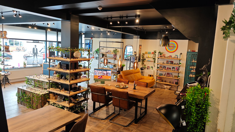 A modern, open-concept optometry practice with wooden displays of eyewear, wrapped in leaves. Desks are spread out alongside sofas for consultations