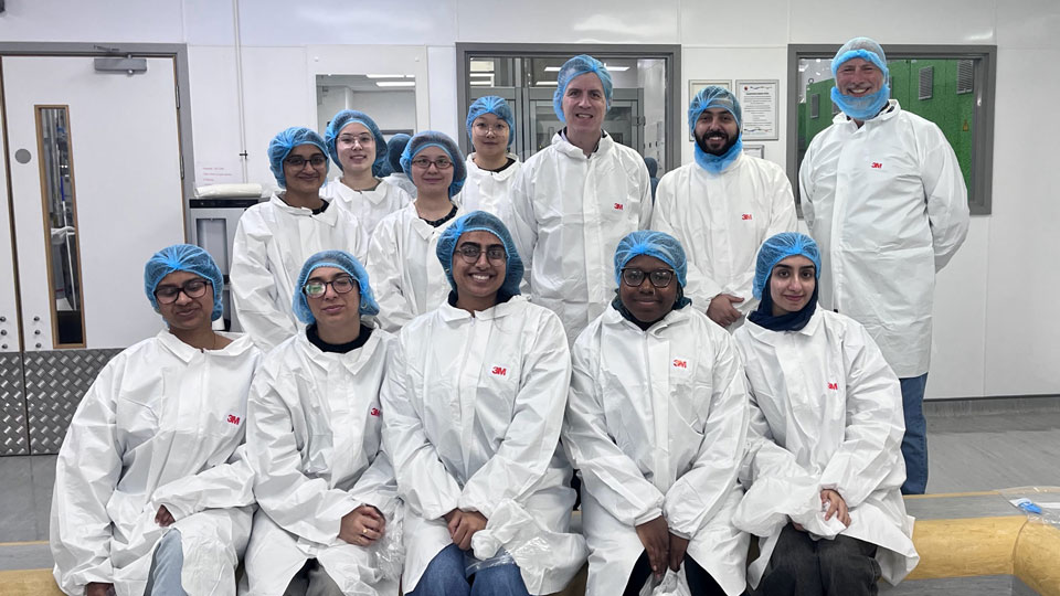A group of students, along with Professor Philip Morgan and Neil Harvey are dressed in white protective boiler suits in the manufacturing facility 