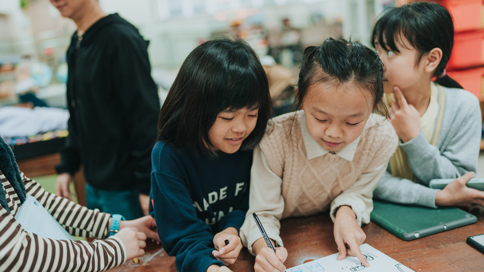 A group of school children gather around a desk to draw